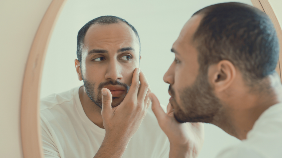 Man examining his face in a round mirror