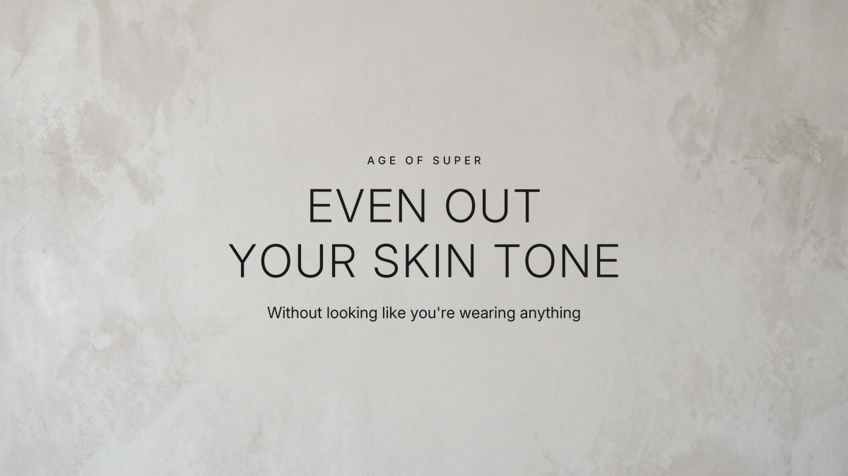 Centered text "Even out your skin tone" with the line "Without looking like you're wearing anything" on a smooth warm gray stone surface that is mottled at the edges and even in the center