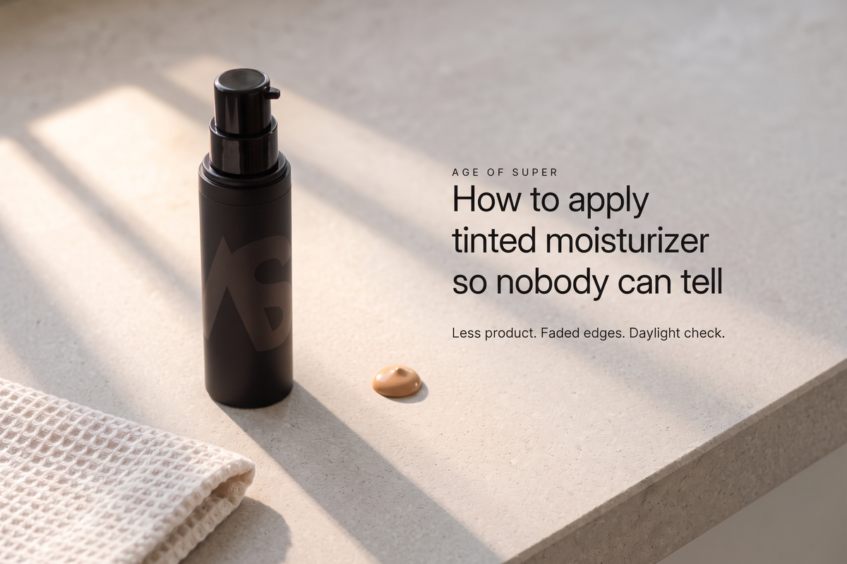 Text "How to apply tinted moisturizer so nobody can tell" beside a black Stealth Blender pump bottle and a pea-sized dot of tint on a pale stone counter in morning window light, with a folded waffle towel