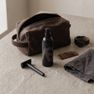 Stealth Blender men's tinted moisturizer on a bathroom counter with a canvas dopp kit, safety razor, comb and watch